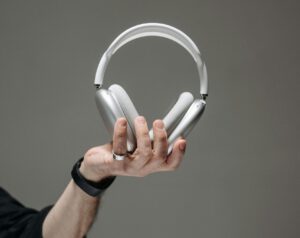 Hand hält weißen Kopfhörer vor grauem Hintergrund, Titelbild für Podcastfolge Trauer am Arbeitsplatz