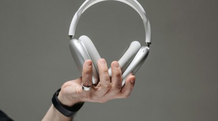 Hand hält weißen Kopfhörer vor grauem Hintergrund, Titelbild für Podcastfolge Trauer am Arbeitsplatz